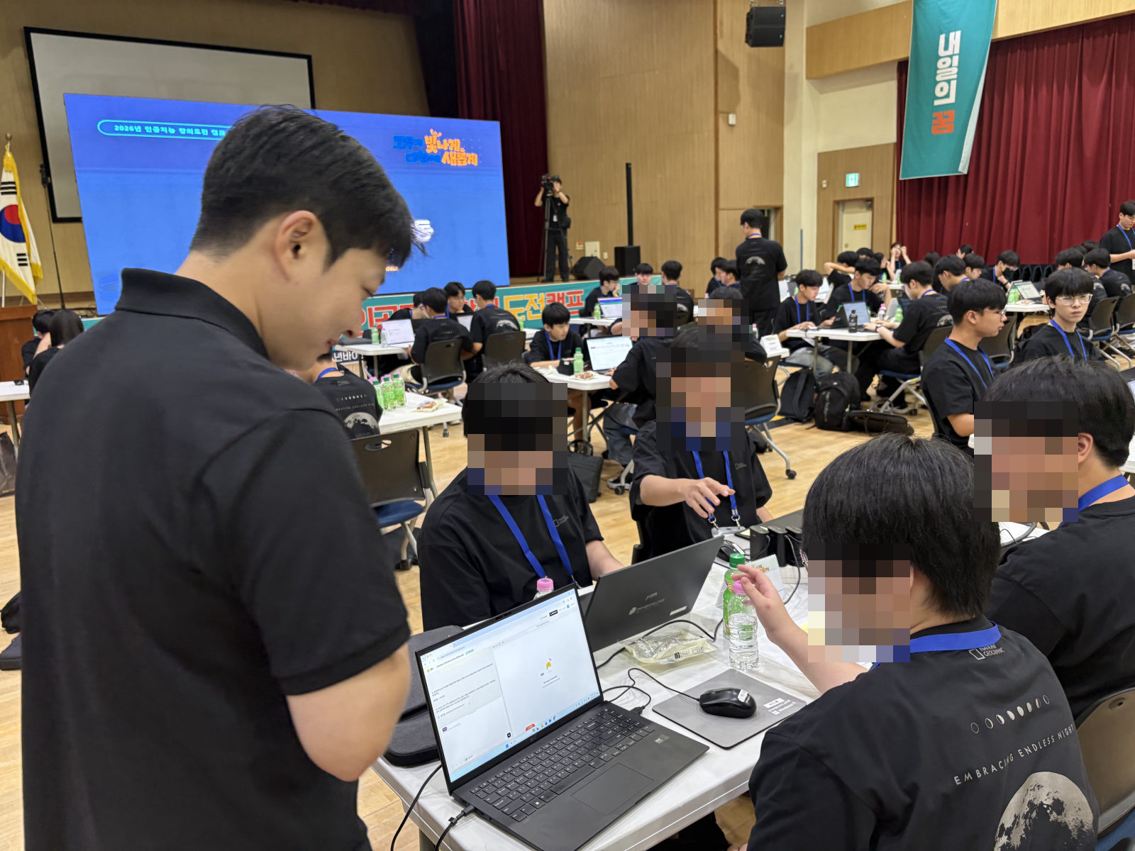 강사가 학생 팀 자리에 서서 화면을 함께 보며 도와주는 모습